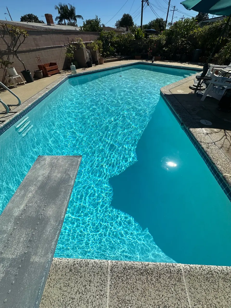 Sparkling turquoise pool with a diving board, entry steps, tiled edges, and surrounding potted plants, after pool service in Torrance, CA