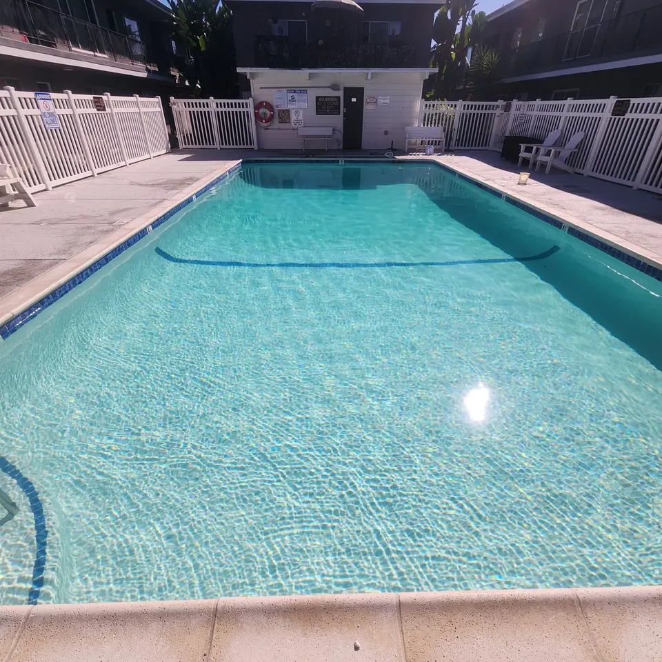 Rectangular pool with sparkling turquoise water, blue tile trim, entry steps, and white perimeter fencing, after pool service in Torrance, CA