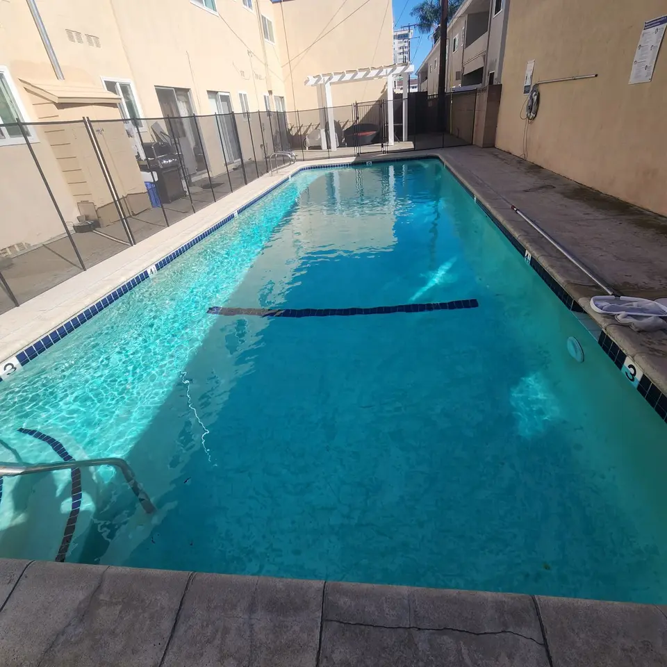 Clear turquoise water fills a rectangular pool with blue tile trim, lane markings, and a metal entry handrail, after pool service in Torrance, CA