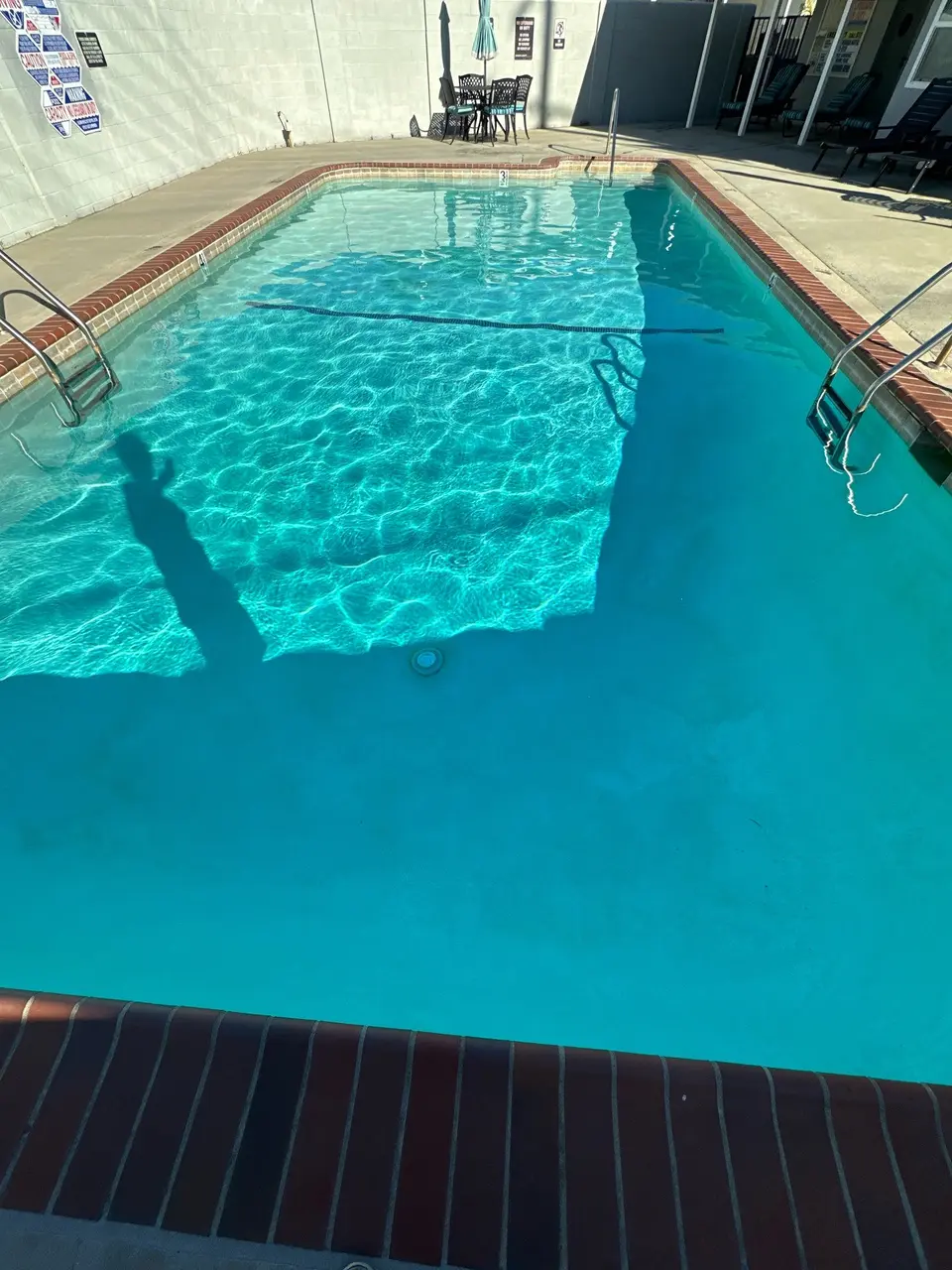Clear turquoise water fills a rectangular pool with brick coping, metal ladders, and poolside seating, after pool service in Torrance, CA