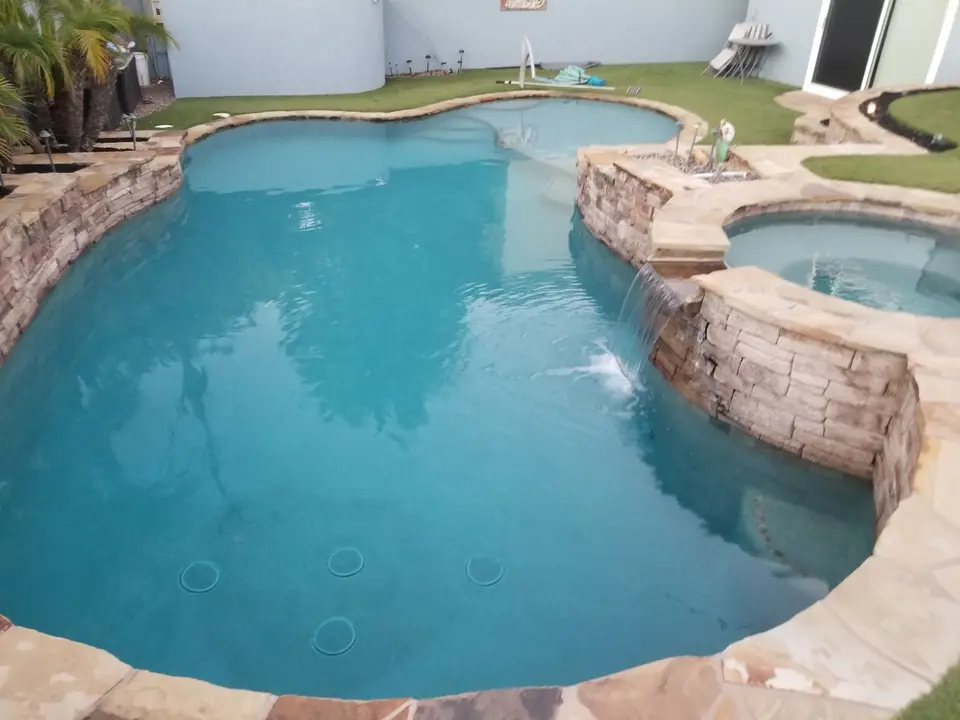 Clear turquoise pool with a raised stone spa, spillover waterfall, shallow sun shelf, and palm landscaping, after pool service in Torrance, CA
