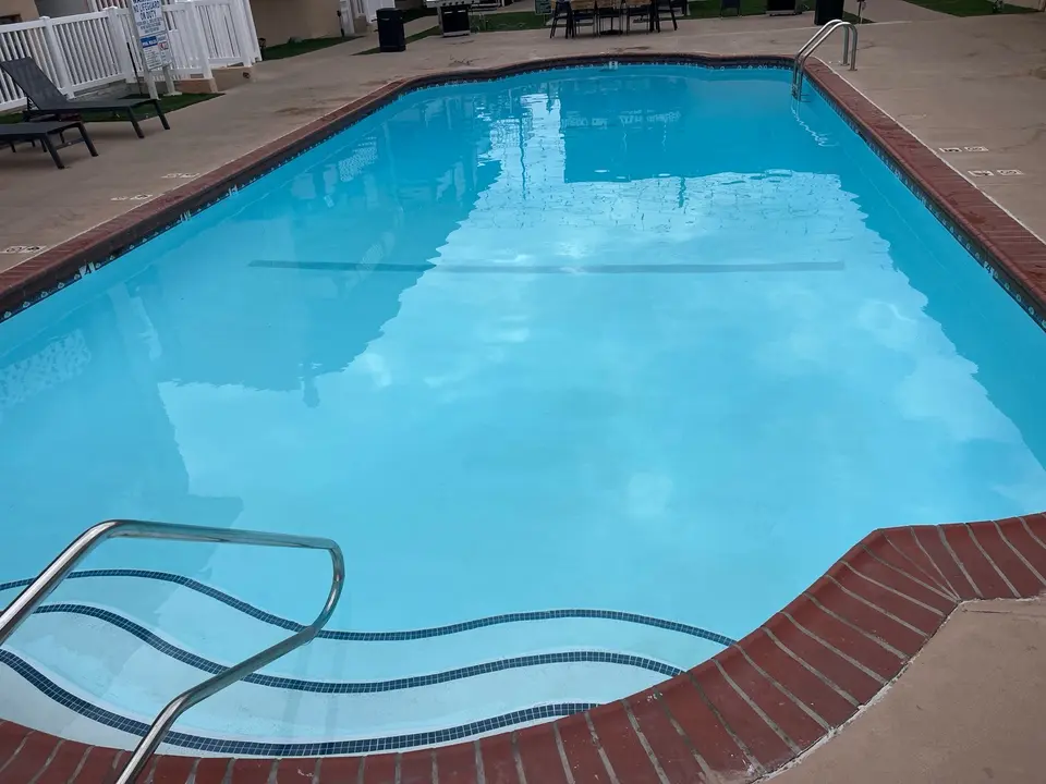 Clear blue pool water reveals tiled entry steps, with stainless steel handrails, brick coping, and poolside seating, after pool service in Torrance, CA