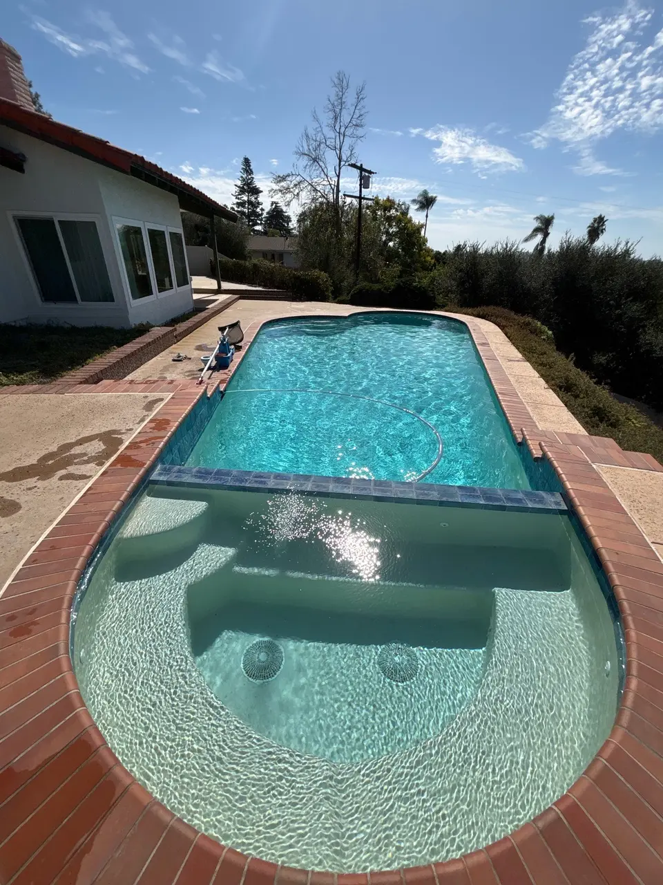Sparkling turquoise pool with an attached spa, submerged benches, brick coping, and surrounding landscaping, after pool service in Vista, CA