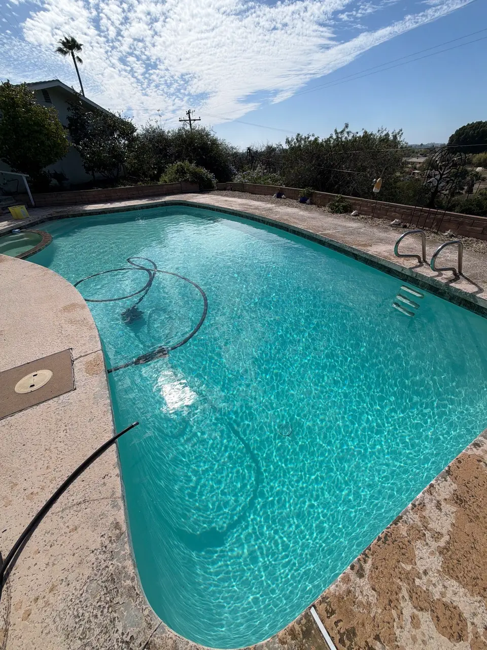 Sparkling turquoise pool with an attached rounded spa, entry steps, metal ladder, and textured concrete deck, after pool service in Vista, CA