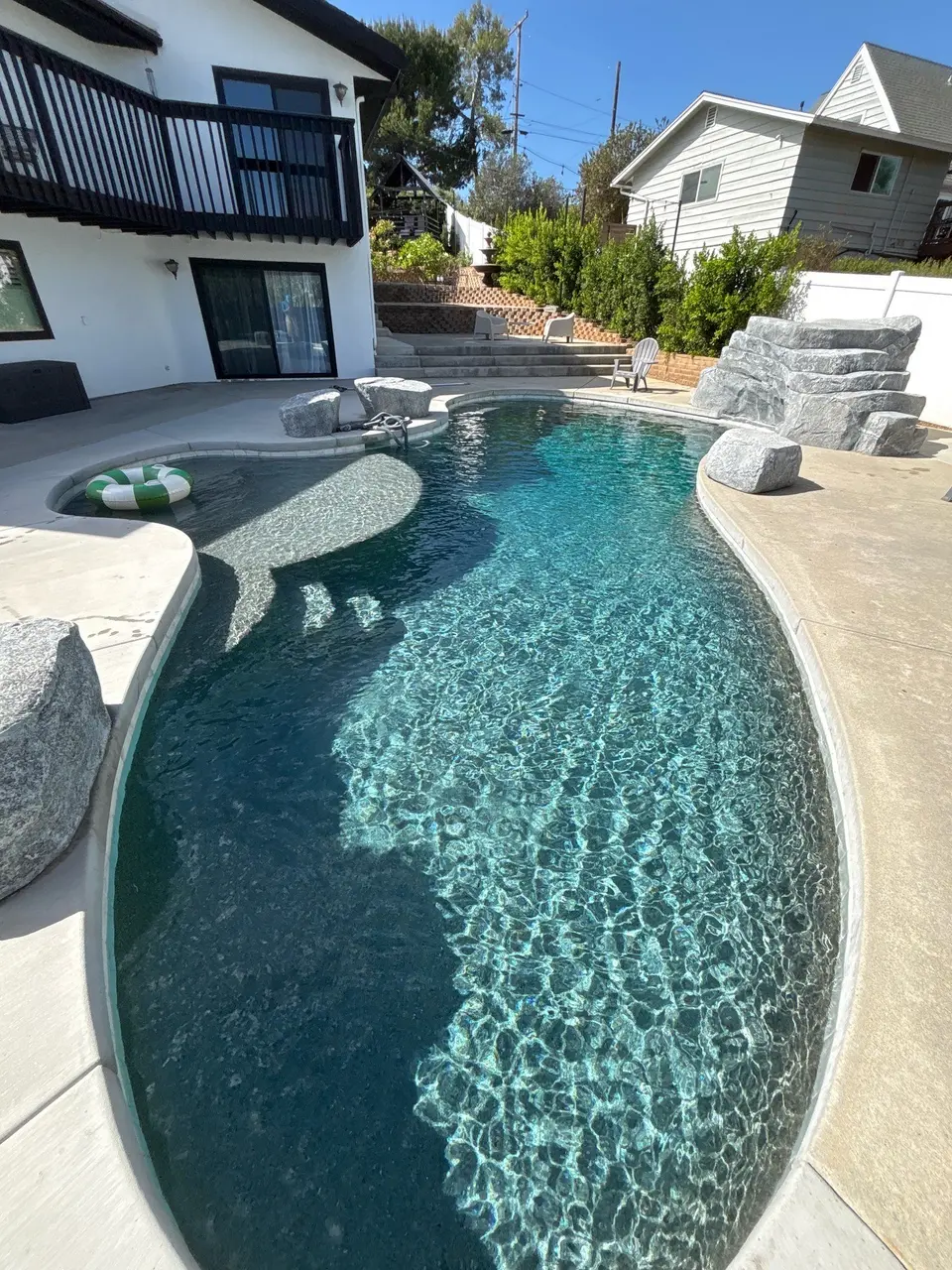 Sparkling turquoise water fills a freeform pebble-finish pool with a shallow shelf and decorative rock waterfall, after pool service in Vista, CA