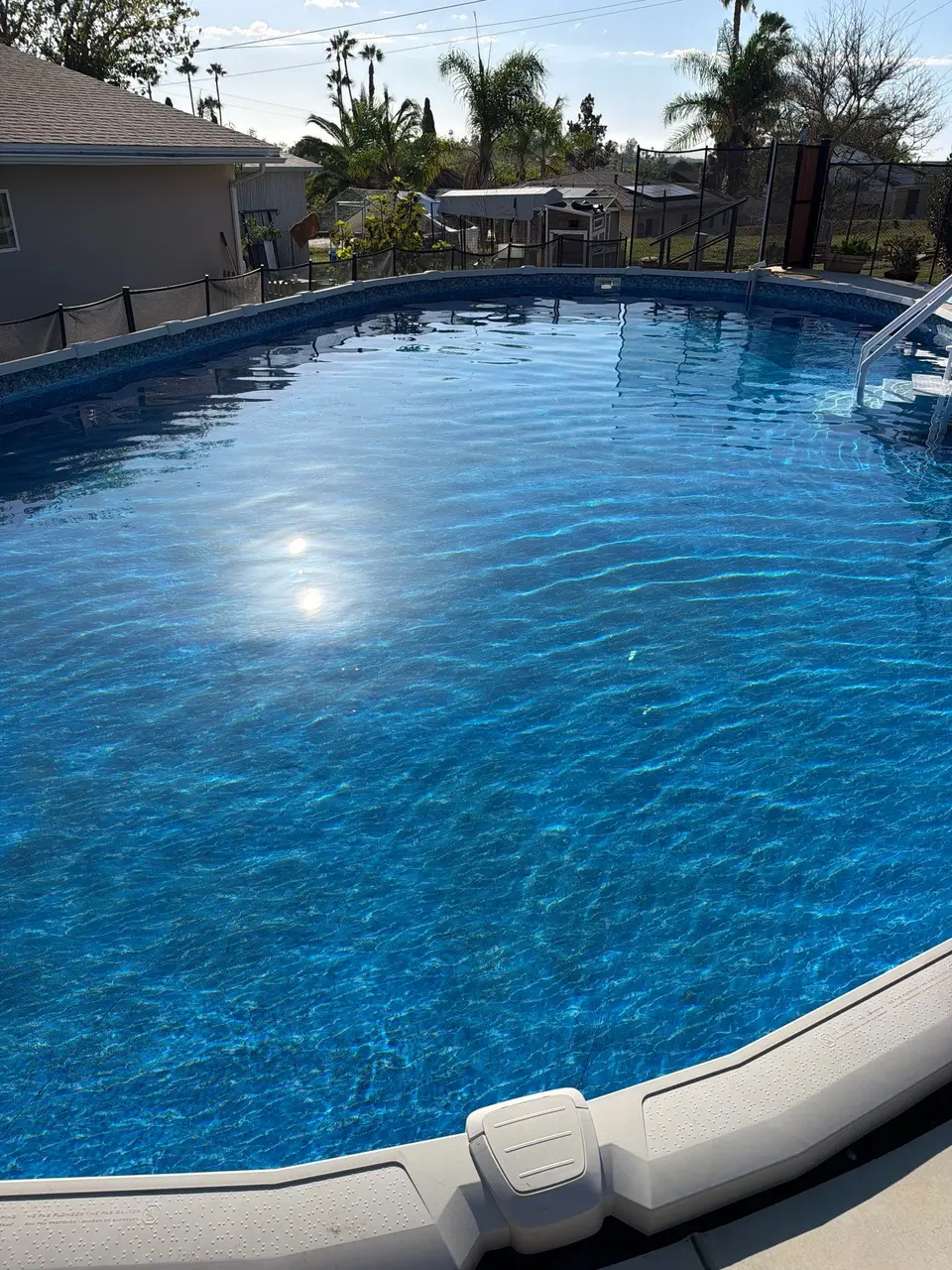 Sparkling blue water fills an above-ground pool with a patterned liner, entry steps, and metal handrail, after pool service in Vista, CA