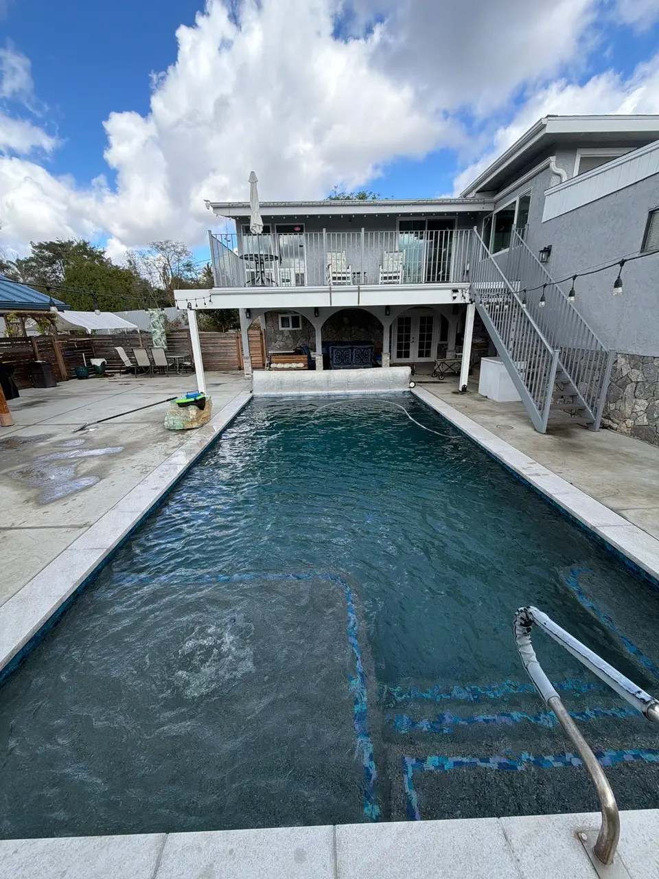 Clear, deep teal water fills a rectangular pool with an integrated spa, blue tile accents, and entry steps, after pool service in Vista, CA