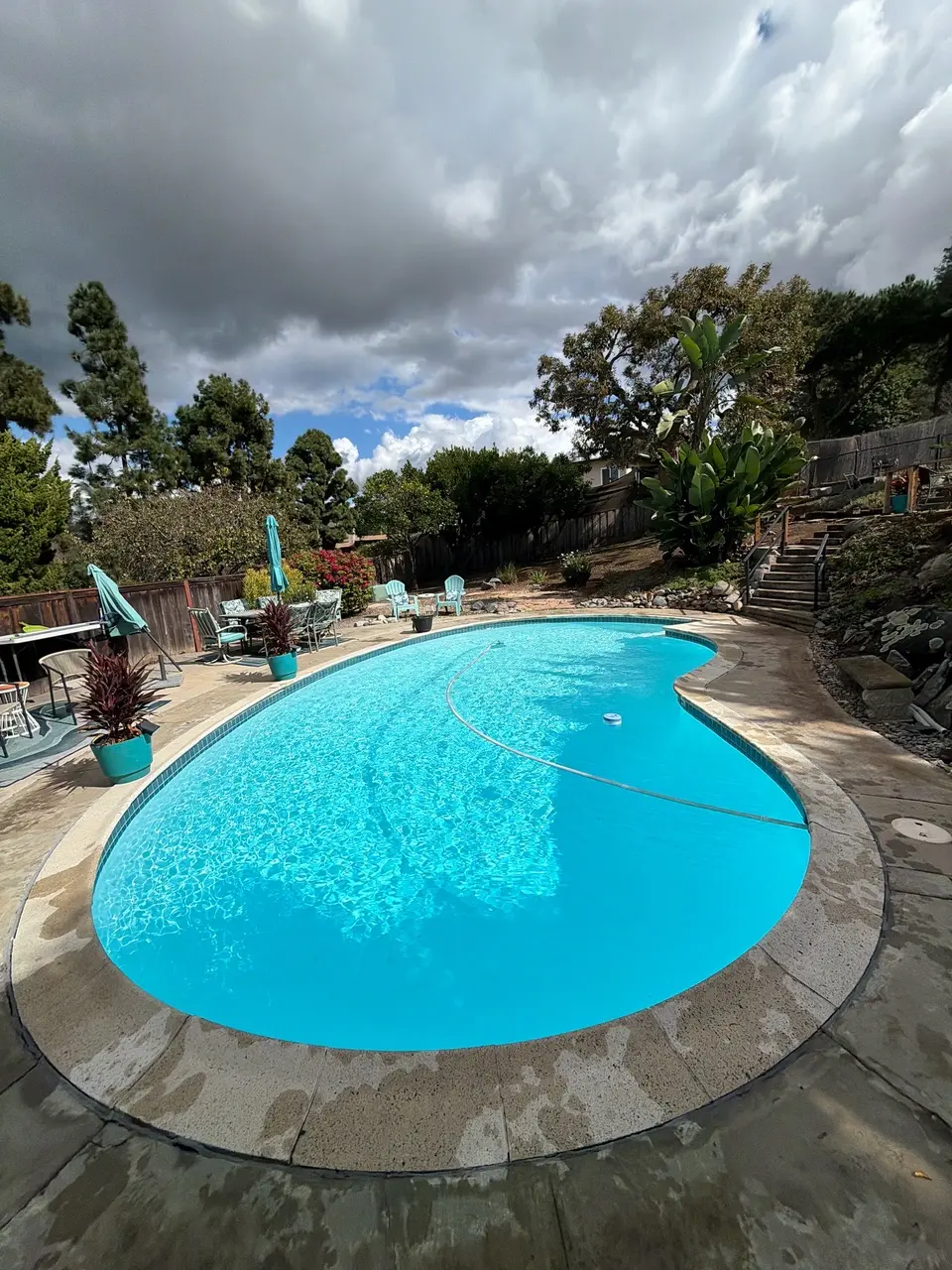 Sparkling turquoise water fills a freeform pool surrounded by stone coping, patio seating, and lush landscaping, after pool service in Vista, CA