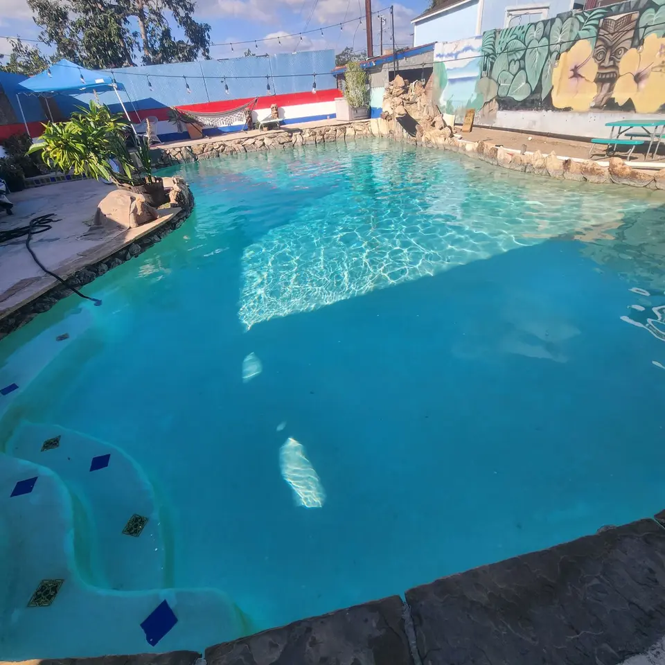 Clear turquoise pool with curved tiled steps, rock coping, a rock waterfall structure, and tropical murals, after pool service in Wilmington, CA